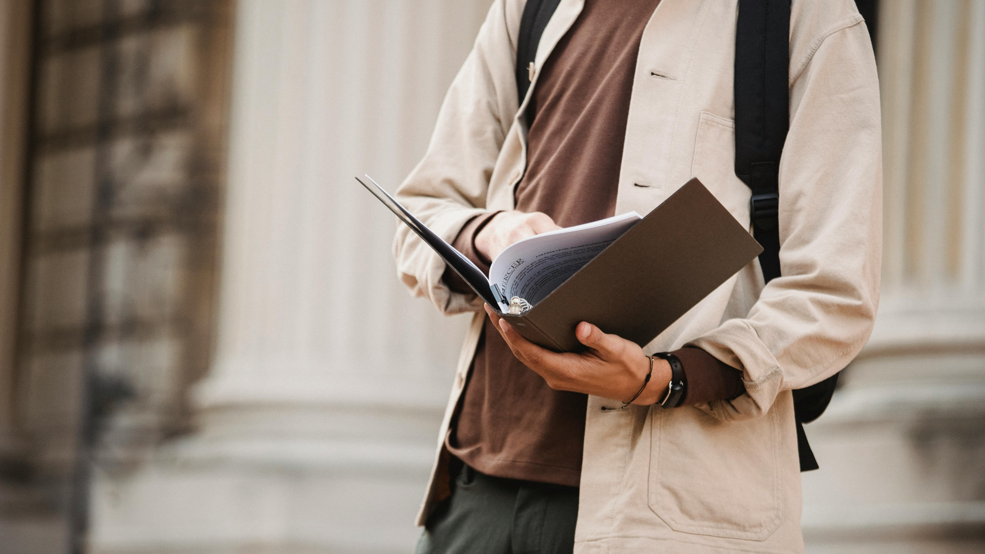 Student wearing backpack holding a binder of papers